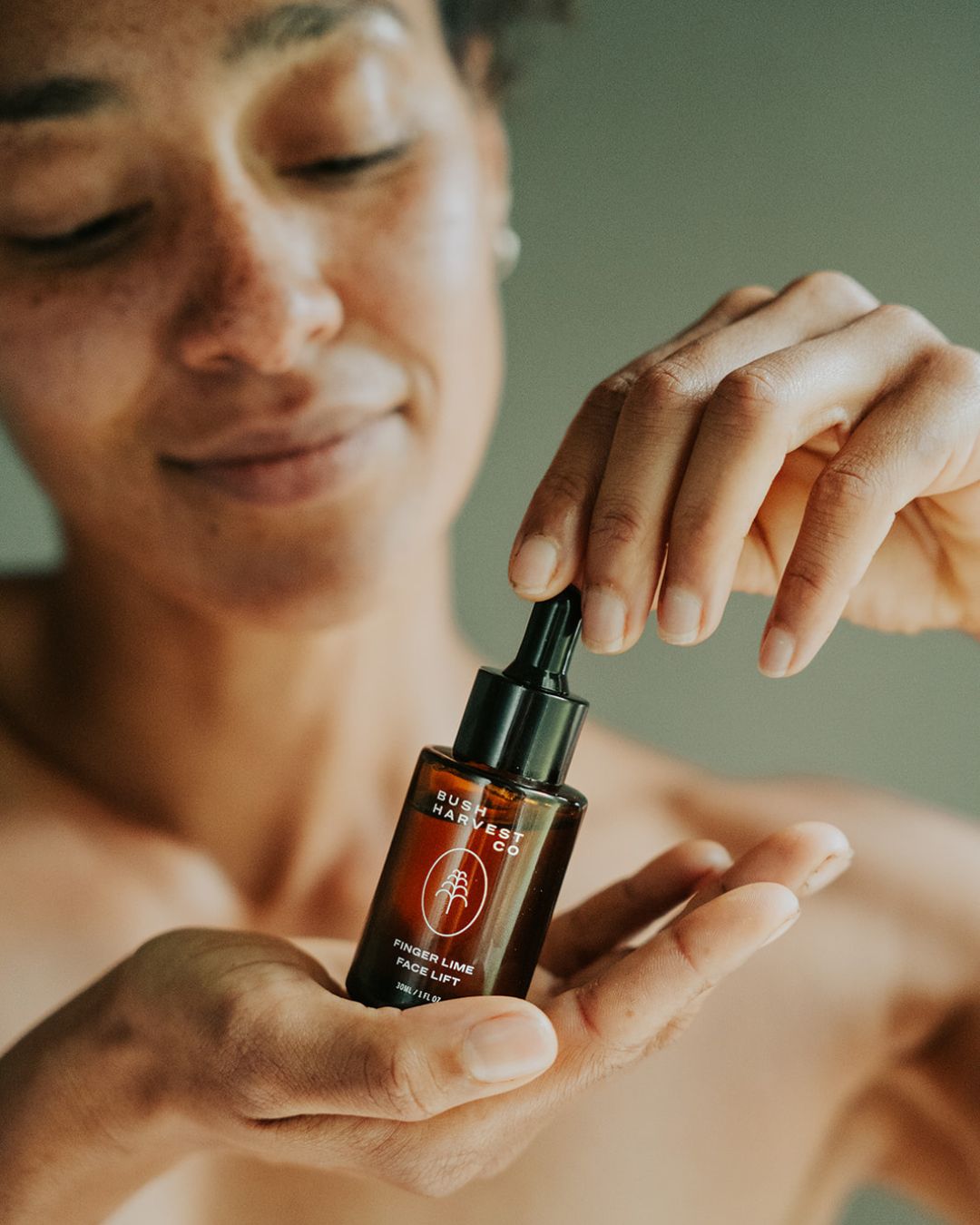 Woman holding Finger Lime Face Lift Hydrating & Brightening Serum bottle.