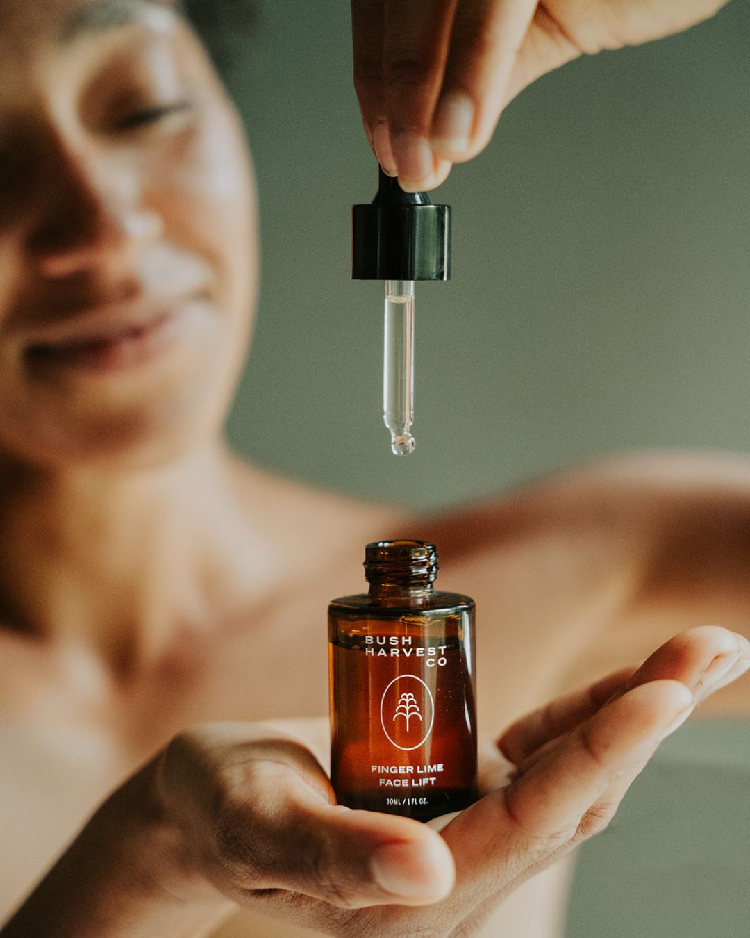 Woman holding Finger Lime Face Lift Hydrating & Brightening Serum bottle and dropper.