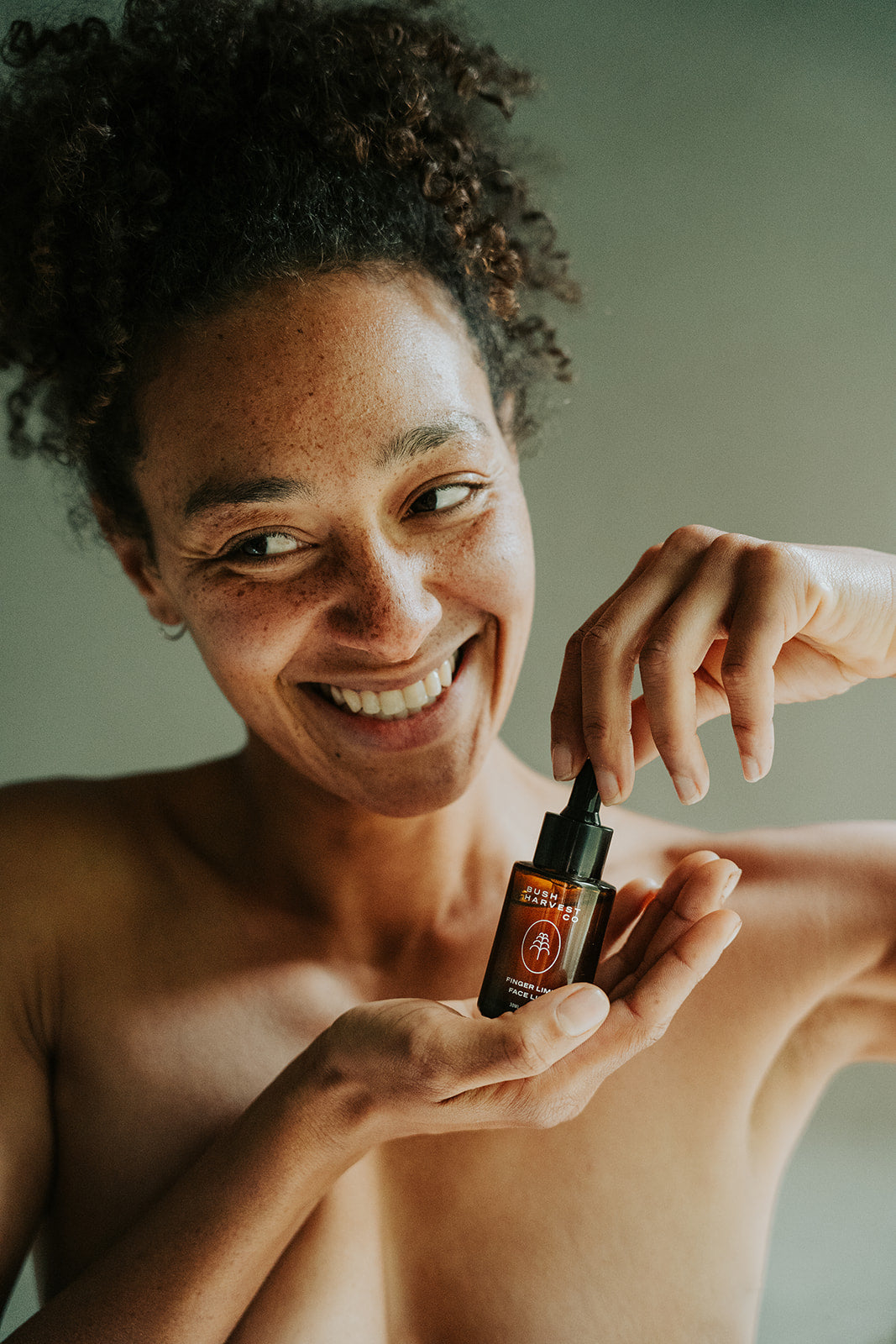 Smiling woman holding Finger Lime Face Lift Hydrating & Brightening Face Serum bottle.