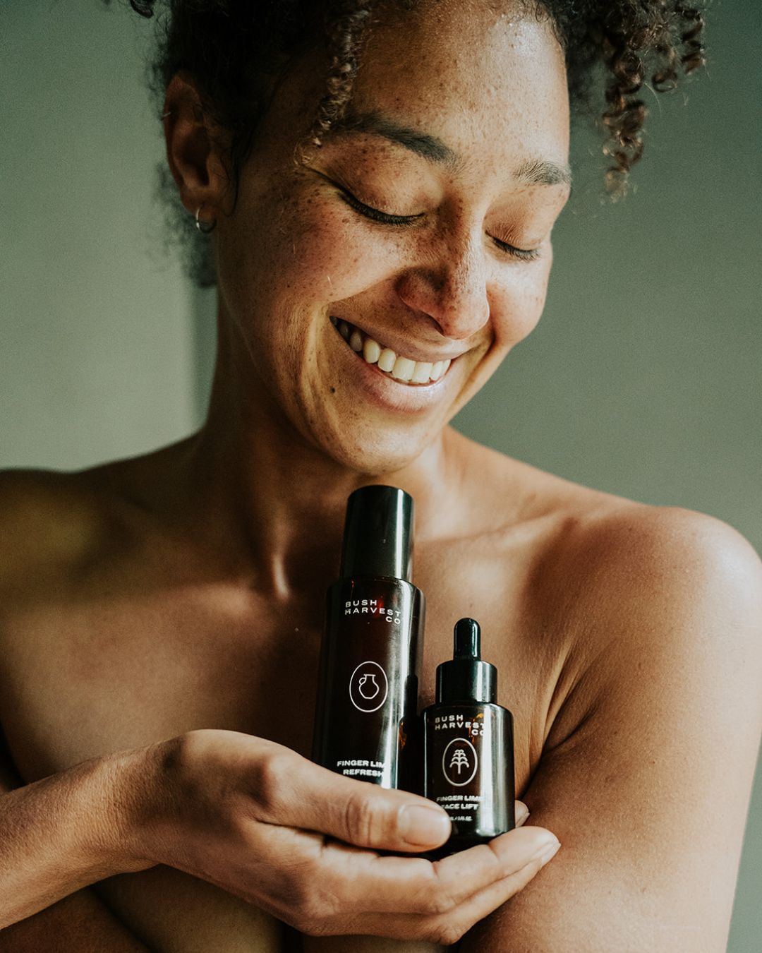 Smiling woman holding Finger Lime Refresh Purifying Facial Cleanser and Finger Lime Face Lift Hydrating & Brightening Serum bottles in hand.