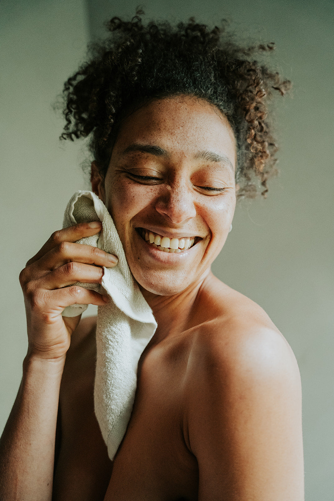 Smiling woman holding reusable, bamboo cotton blend Facial Cleansing Cloth to cheek.