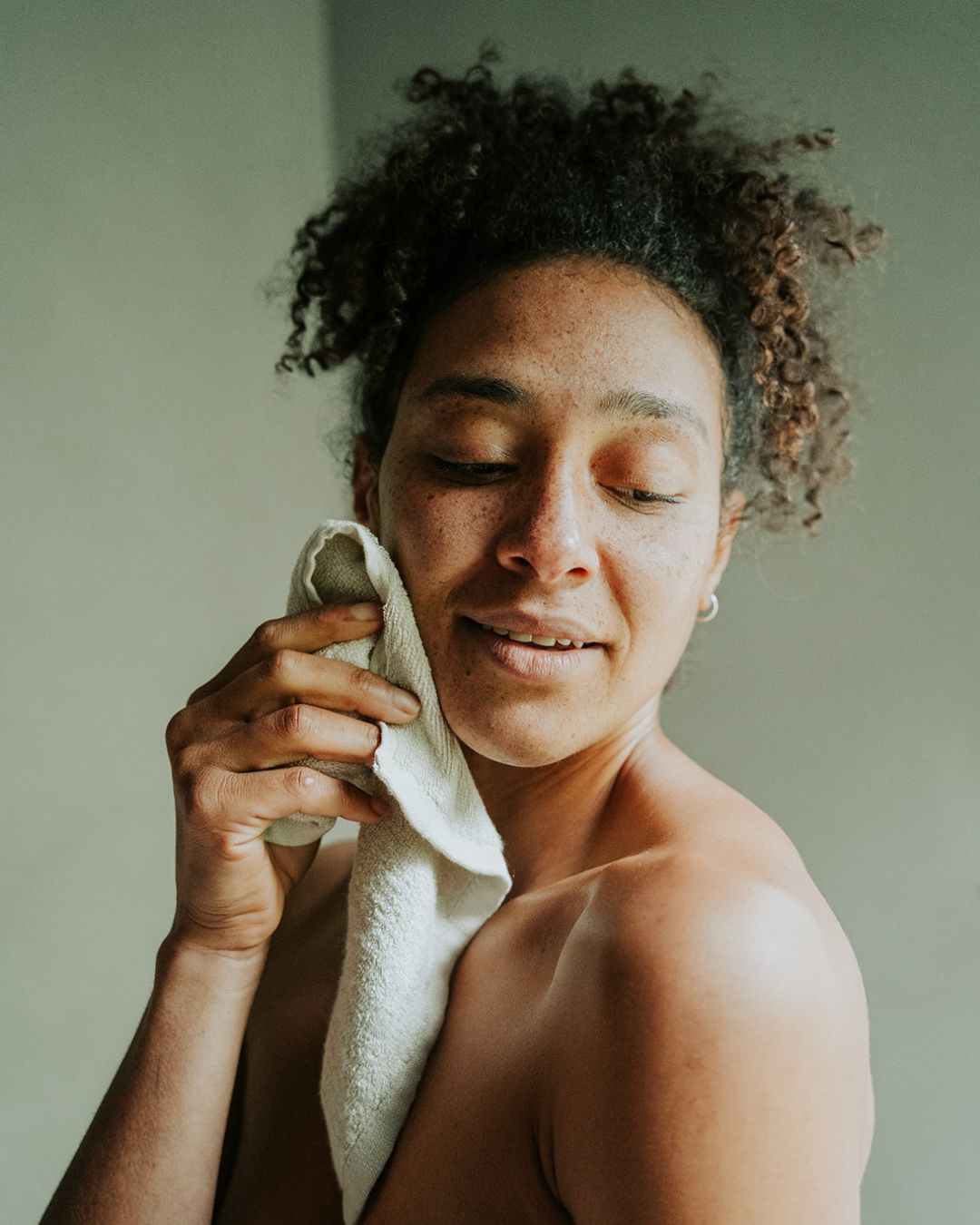 Woman holding resuable, bamboo cotton blend Facial Cleansing Cloth to cheek.