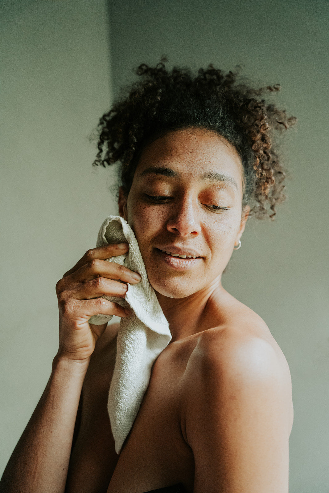 Woman holding reusable, bamboo cotton blend Facial Cleansing Cloth to face.