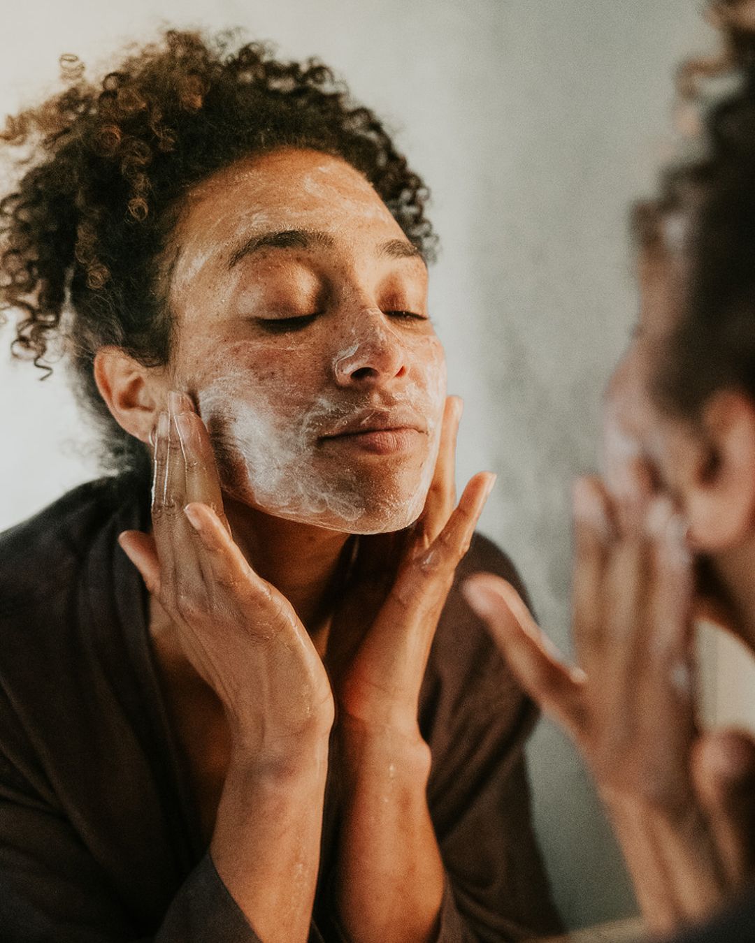 Woman facing mirror and applying Finger Lime Refresh Purifying Facial Cleanser to her face.